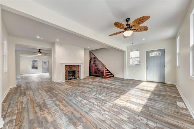 unfurnished living room featuring stairs, a brick fireplace, baseboards, and wood finished floors