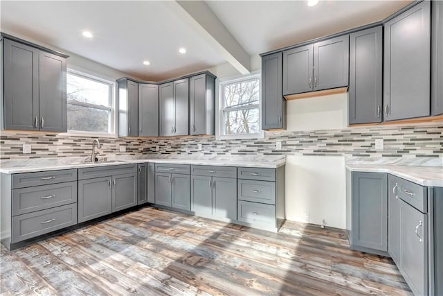 kitchen with light wood-style flooring, gray cabinets, a sink, and beamed ceiling