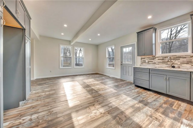 kitchen with tasteful backsplash, gray cabinets, a sink, and light wood-style flooring