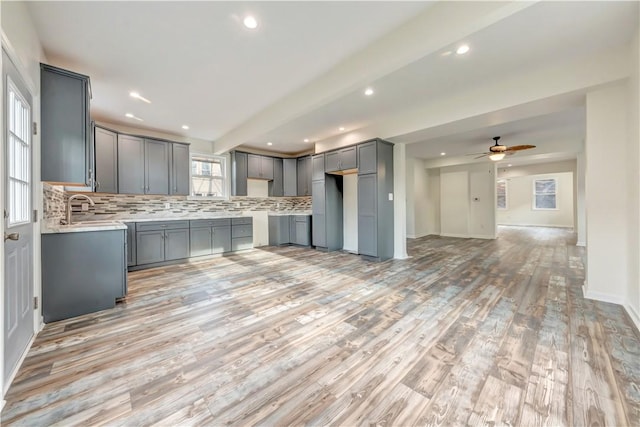 kitchen with gray cabinets, a sink, backsplash, and open floor plan