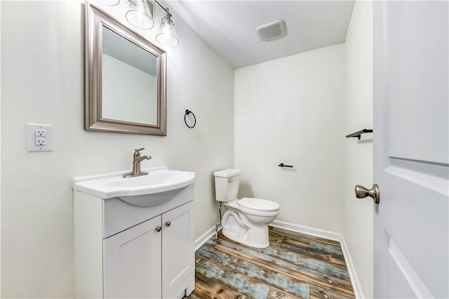 half bathroom featuring toilet, wood finished floors, vanity, and baseboards