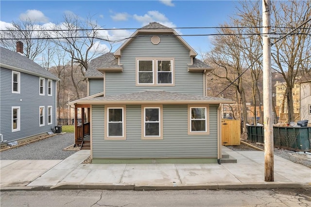 view of front of home with central air condition unit, fence, and roof with shingles