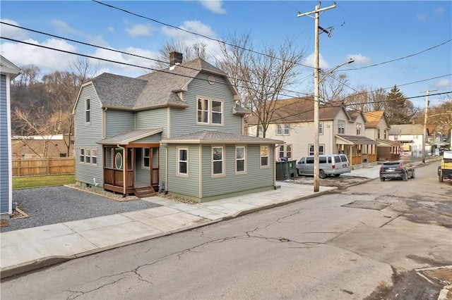 view of front of house featuring a shingled roof, a residential view, fence, and a chimney