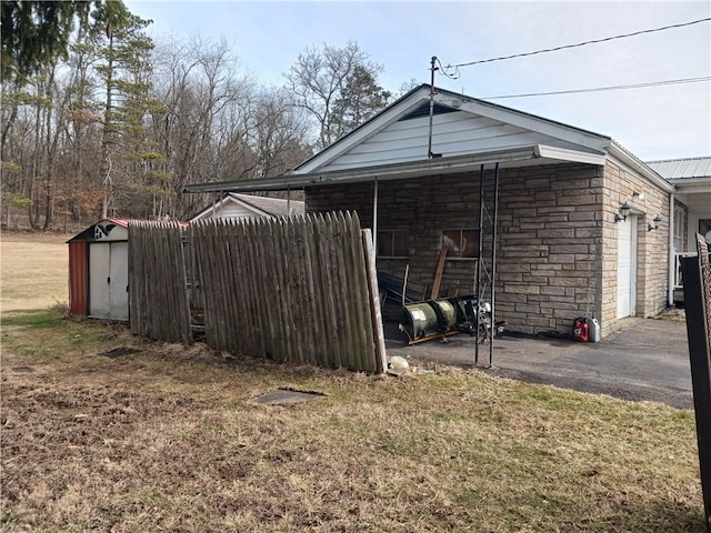 view of side of home featuring a storage shed, a garage, an outdoor structure, stone siding, and driveway