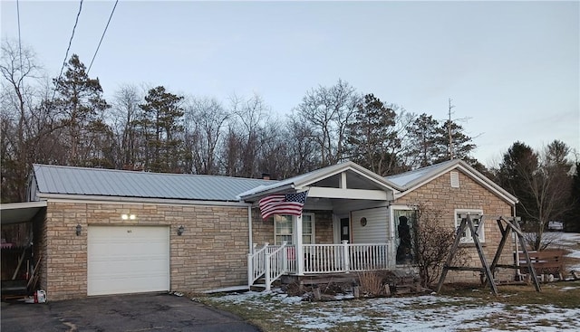 ranch-style house featuring a garage, covered porch, metal roof, and aphalt driveway