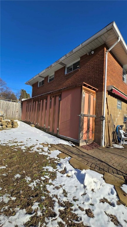 snow covered back of property featuring fence and brick siding