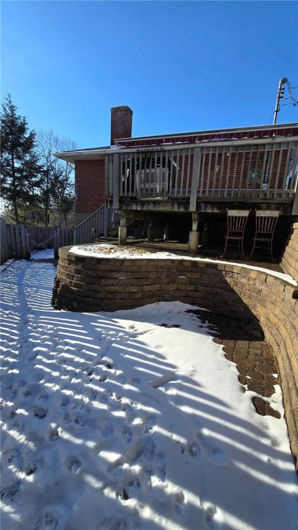 snow covered rear of property with a chimney, fence, and a deck