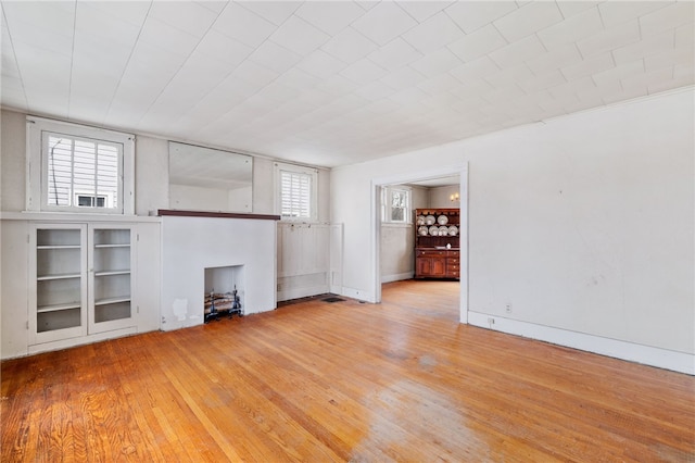 unfurnished living room with baseboards, light wood-style flooring, and a healthy amount of sunlight