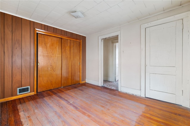 unfurnished bedroom featuring wood walls, a closet, wood finished floors, and visible vents