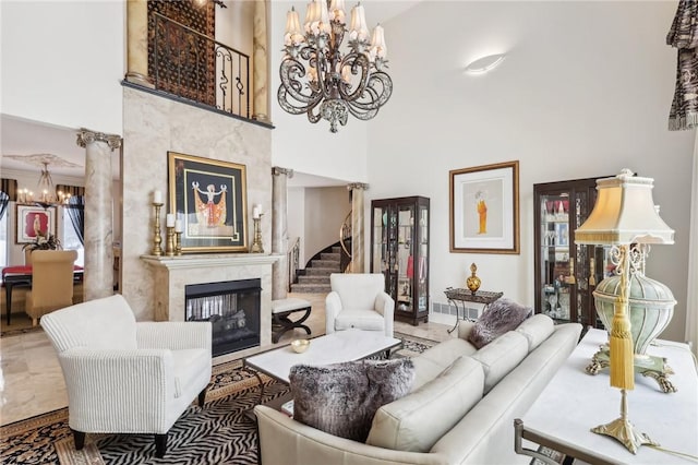 living area with a high ceiling, stairs, ornate columns, a fireplace, and a chandelier