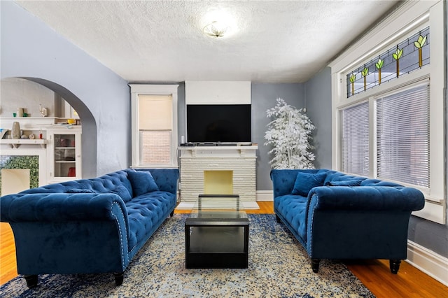 living room with arched walkways, a fireplace, a textured ceiling, wood finished floors, and baseboards