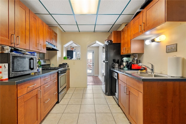 kitchen featuring brown cabinets, stainless steel appliances, dark countertops, a sink, and under cabinet range hood