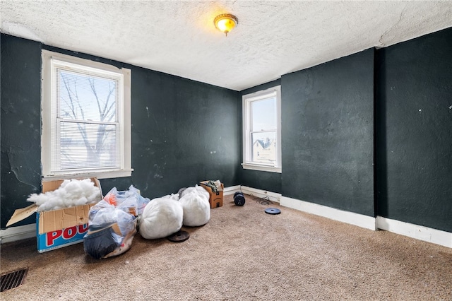 empty room with carpet floors, visible vents, a textured ceiling, and baseboards