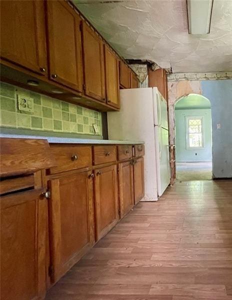 kitchen featuring arched walkways, light countertops, brown cabinetry, freestanding refrigerator, and light wood-type flooring