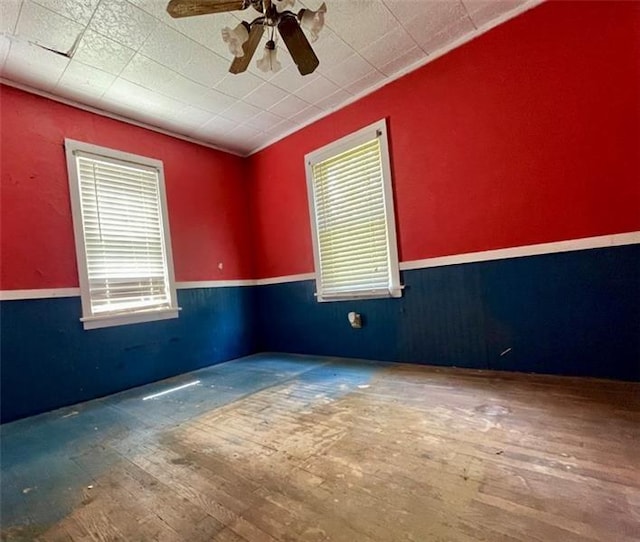 empty room with ceiling fan, wood finished floors, and wainscoting