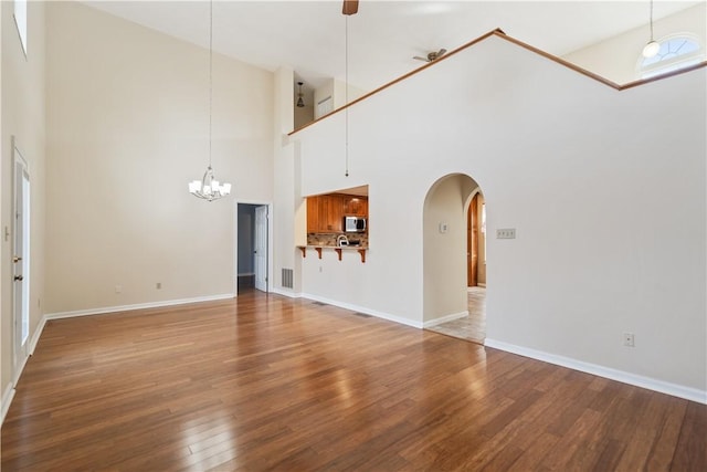 unfurnished living room with arched walkways, visible vents, an inviting chandelier, wood finished floors, and baseboards