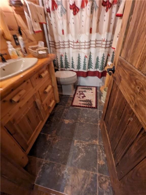 full bath with toilet, stone finish flooring, shower / tub combo with curtain, and vanity