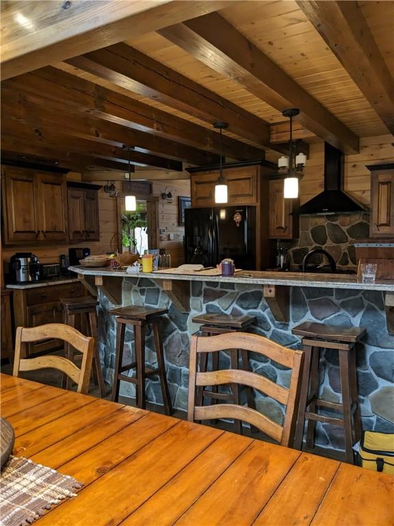 kitchen with a breakfast bar, freestanding refrigerator, hanging light fixtures, and range hood