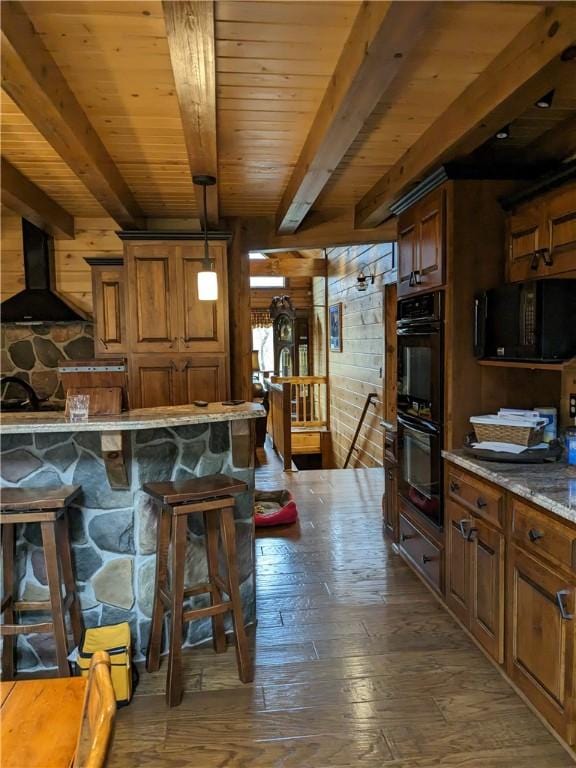 kitchen with a breakfast bar area, dark wood-type flooring, ventilation hood, black appliances, and pendant lighting