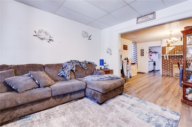 living room with a drop ceiling, a notable chandelier, and wood finished floors