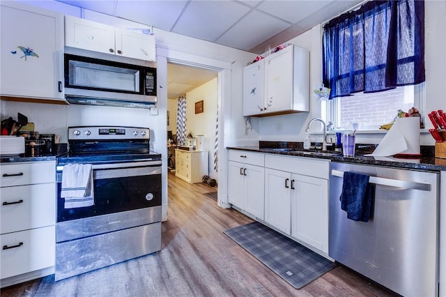 kitchen with light wood finished floors, appliances with stainless steel finishes, white cabinets, a sink, and a drop ceiling