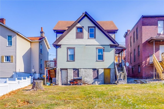 rear view of house with a yard, fence, and stairs