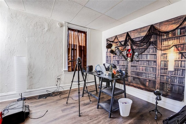 office featuring a textured wall, wood finished floors, a paneled ceiling, and baseboards