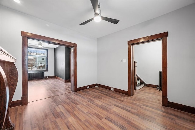 spare room with stairway, radiator heating unit, wood finished floors, and a ceiling fan