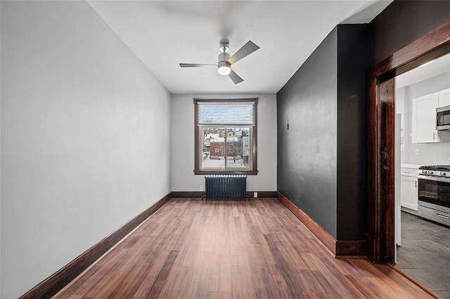 unfurnished room with dark wood-style floors, baseboards, and radiator heating unit