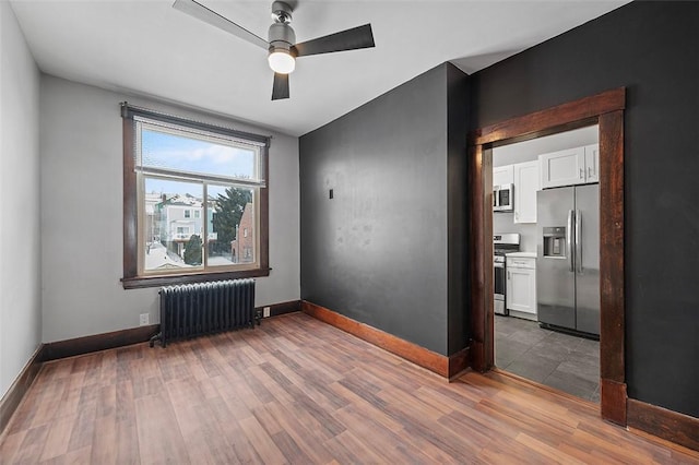 empty room featuring baseboards, wood finished floors, a ceiling fan, and radiator