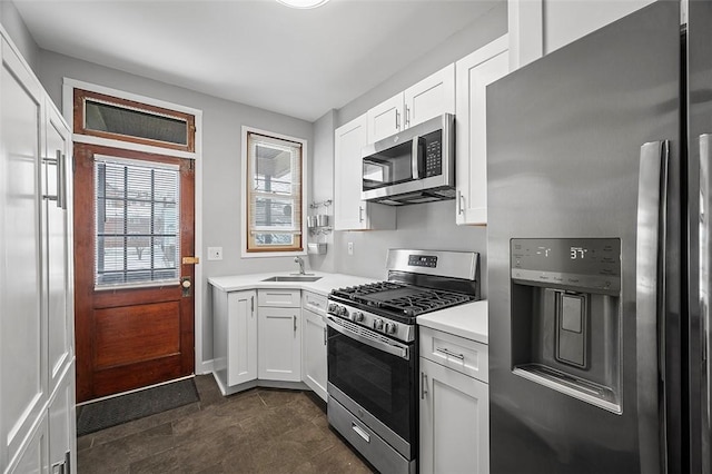 kitchen with appliances with stainless steel finishes, light countertops, a sink, and white cabinetry