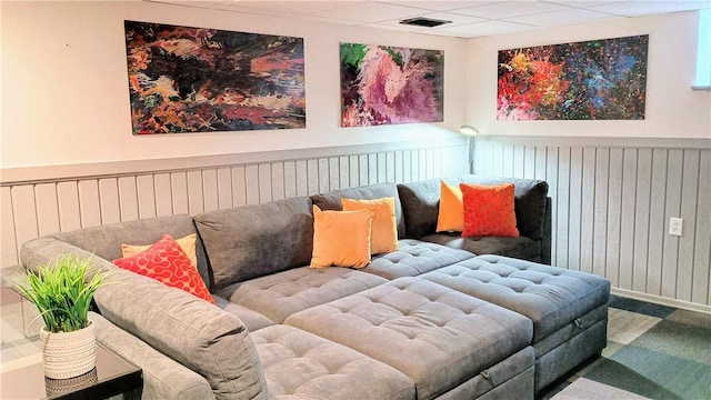 interior space with a paneled ceiling, wood walls, and visible vents