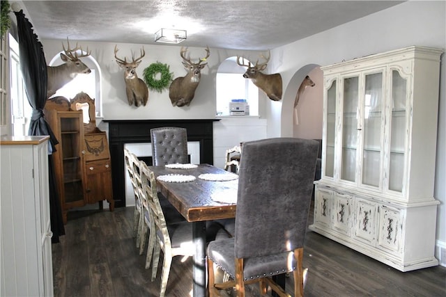 dining area featuring arched walkways, dark wood finished floors, and a textured ceiling