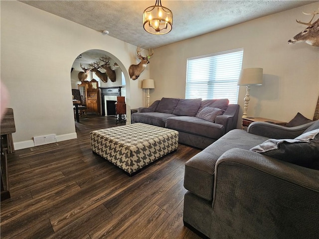 living area with arched walkways, a notable chandelier, visible vents, baseboards, and dark wood-style floors