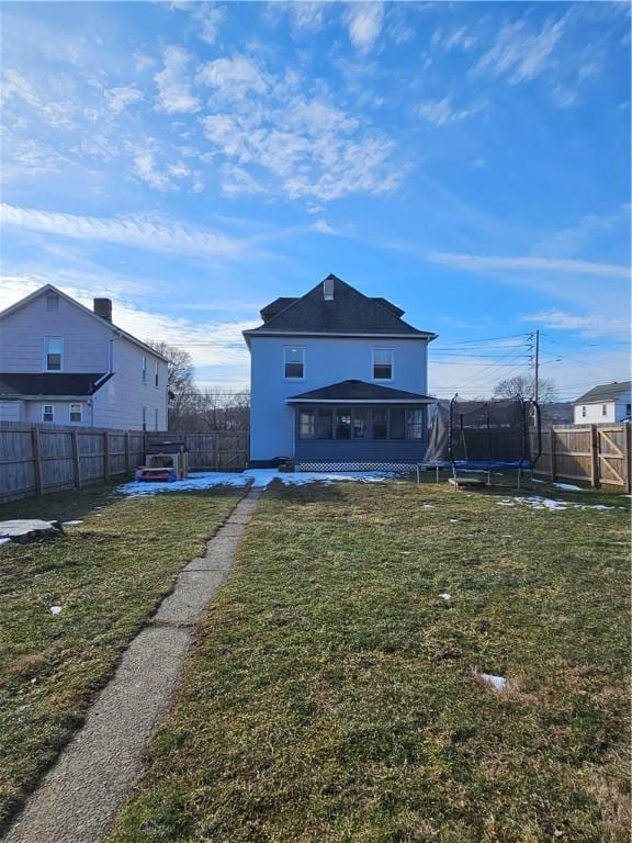 rear view of house featuring a lawn, a trampoline, a fenced backyard, and a sunroom