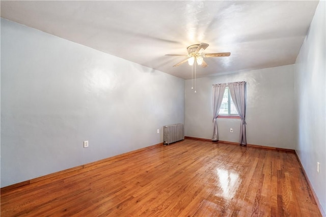 unfurnished room featuring a ceiling fan, radiator, and light wood-style flooring