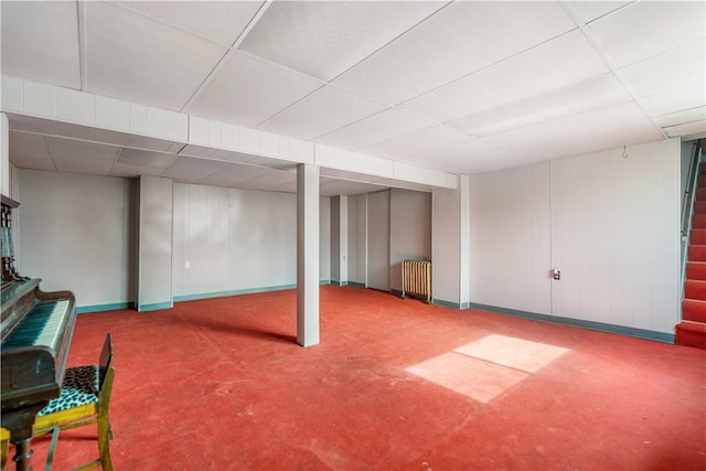 finished below grade area featuring radiator heating unit, a paneled ceiling, and baseboards