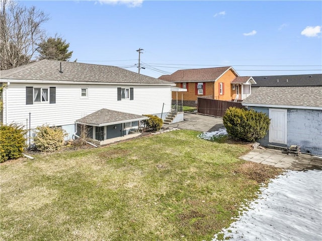 rear view of property featuring a yard, roof with shingles, and fence