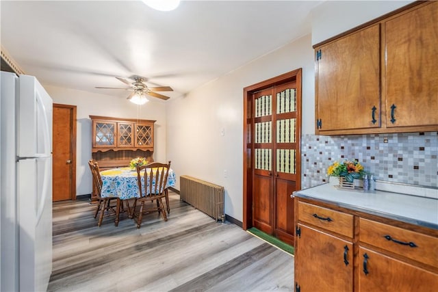 dining area featuring light wood-style floors, radiator heating unit, baseboards, and a ceiling fan