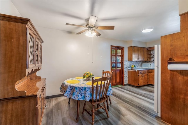 dining room with light wood finished floors, a ceiling fan, and baseboards