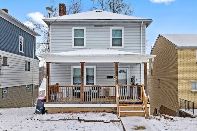 snow covered house with covered porch and a chimney