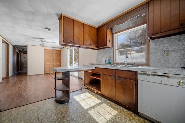 kitchen featuring brown cabinetry, white dishwasher, light countertops, open shelves, and a sink