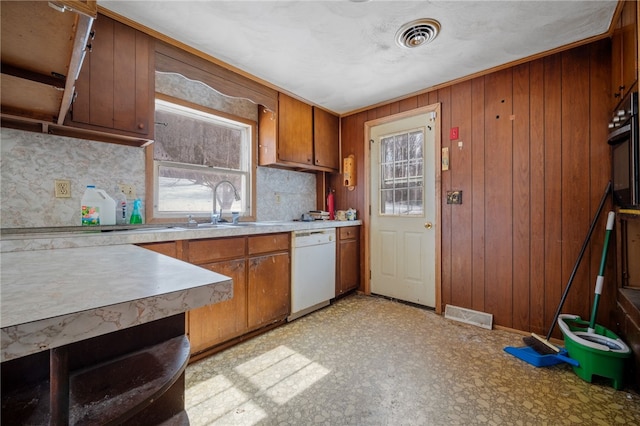 kitchen with wooden walls, a sink, light countertops, dishwasher, and brown cabinetry