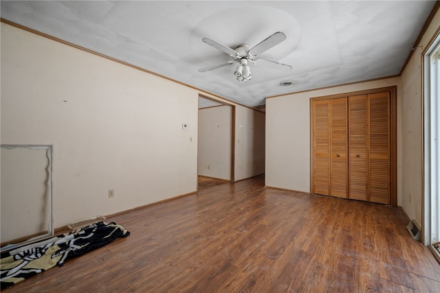 unfurnished bedroom with dark wood-style floors, ceiling fan, ornamental molding, and two closets