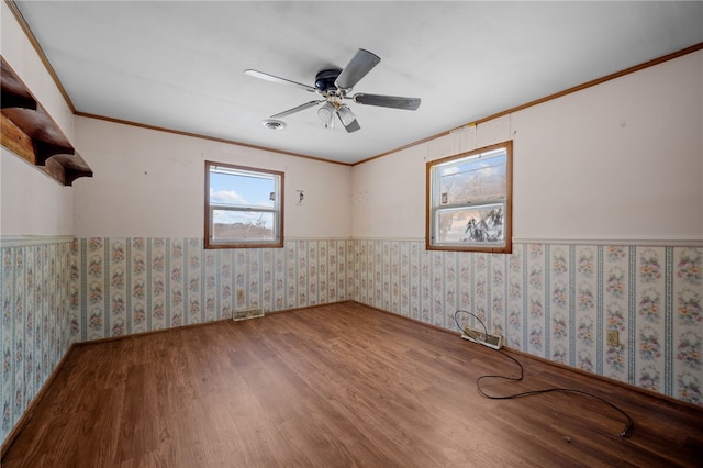 spare room featuring wood finished floors, a ceiling fan, wainscoting, wallpapered walls, and crown molding