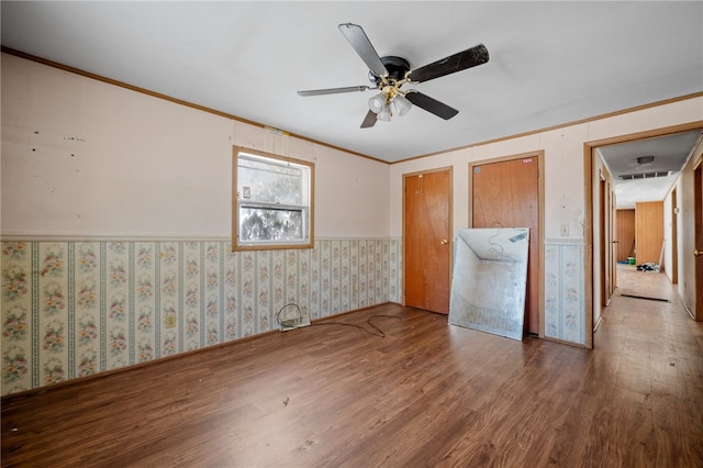 unfurnished bedroom with wood finished floors, visible vents, ornamental molding, wainscoting, and wallpapered walls