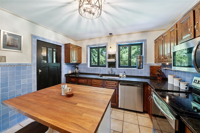 kitchen featuring light tile patterned floors, appliances with stainless steel finishes, decorative light fixtures, a sink, and tile walls