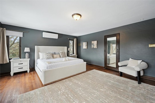 bedroom with an AC wall unit, wood finished floors, and baseboards