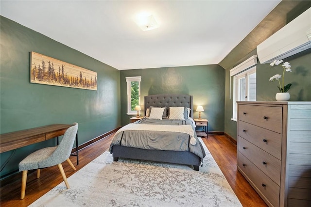 bedroom with baseboards, dark wood finished floors, and an AC wall unit