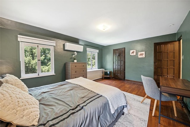 bedroom featuring an AC wall unit, baseboards, radiator heating unit, and wood finished floors